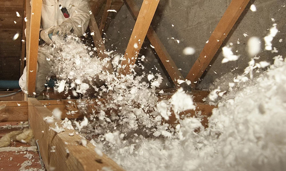 Worker installing blown-in cellulose insulation in attic.