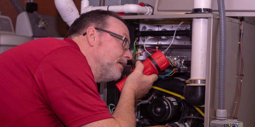 HVAC technician inspecting furnace with flashlight